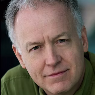 The Freeman Studio A middle-aged man with short gray hair and a slight smile, wearing a green shirt, looks directly at the camera—an inspiring presence at The Freeman Studio. New York & Toronto Acting Studio