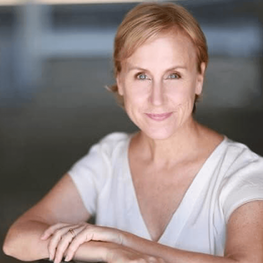 The Freeman Studio A woman with short blonde hair and a light shirt sits with her arms resting in front of her, smiling softly at the camera—a calm presence often seen at The Freeman Studio. New York & Toronto Acting Studio