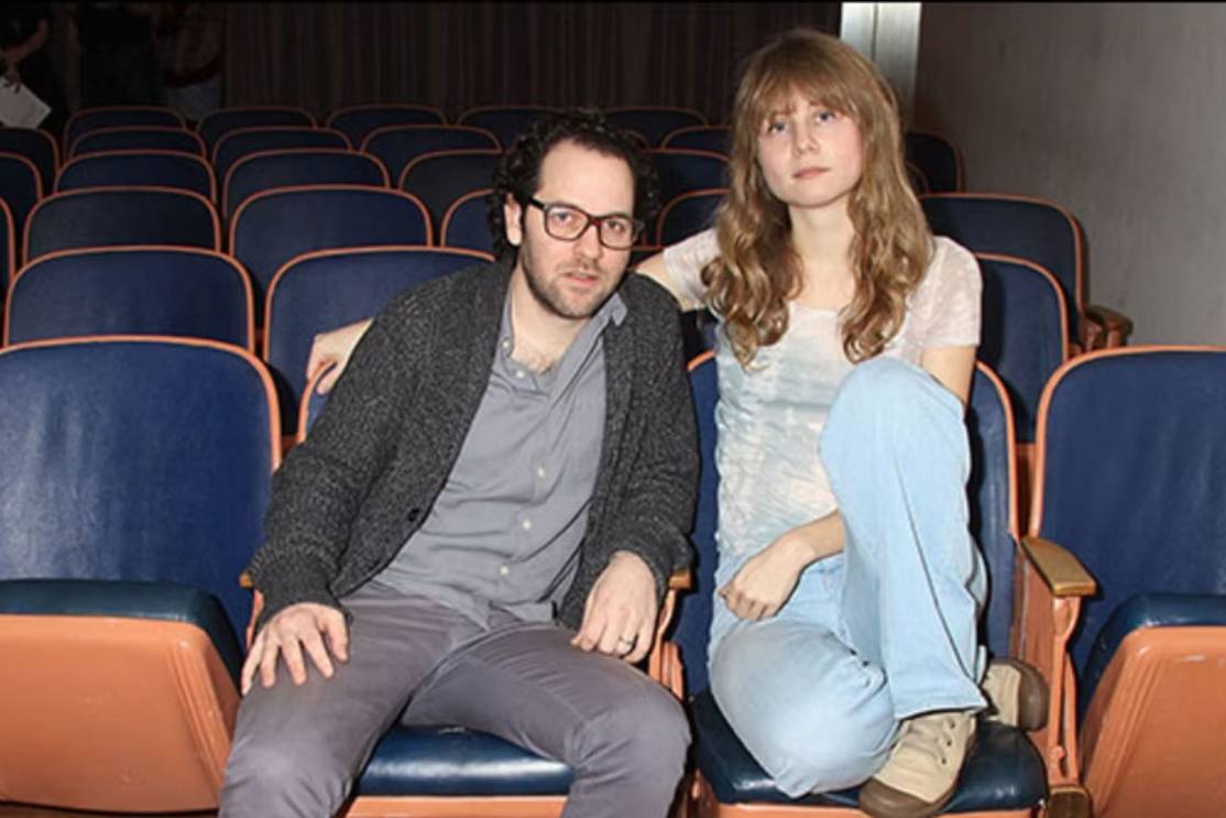 The Freeman Studio Two people, a man and a woman, sit closely together in an empty auditorium with rows of blue and tan seats behind them. New York & Toronto Acting Studio