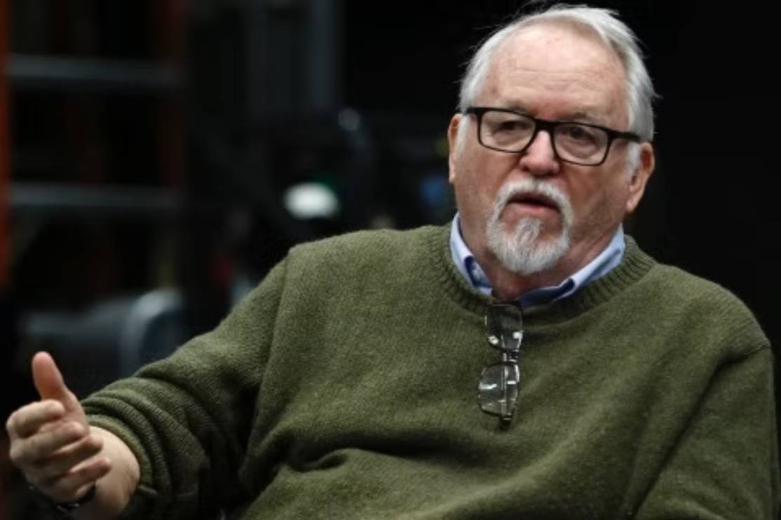 The Freeman Studio An older man with glasses, a gray beard, and a green sweater gestures with his hand while seated indoors. New York & Toronto Acting Studio