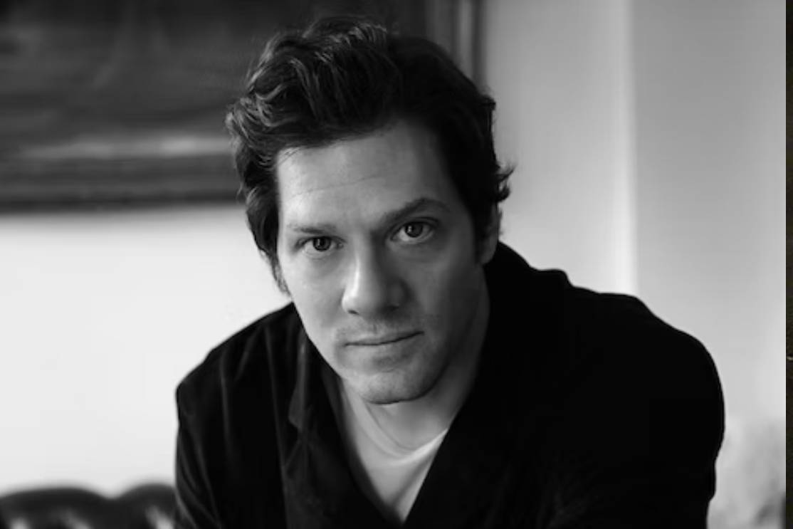 The Freeman Studio A man with dark hair wearing a dark shirt looks directly at the camera in a black and white indoor portrait. New York & Toronto Acting Studio