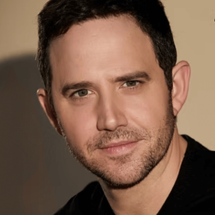The Freeman Studio Man with short dark hair and trimmed beard looking at the camera, wearing a black shirt, against a plain beige background. New York & Toronto Acting Studio