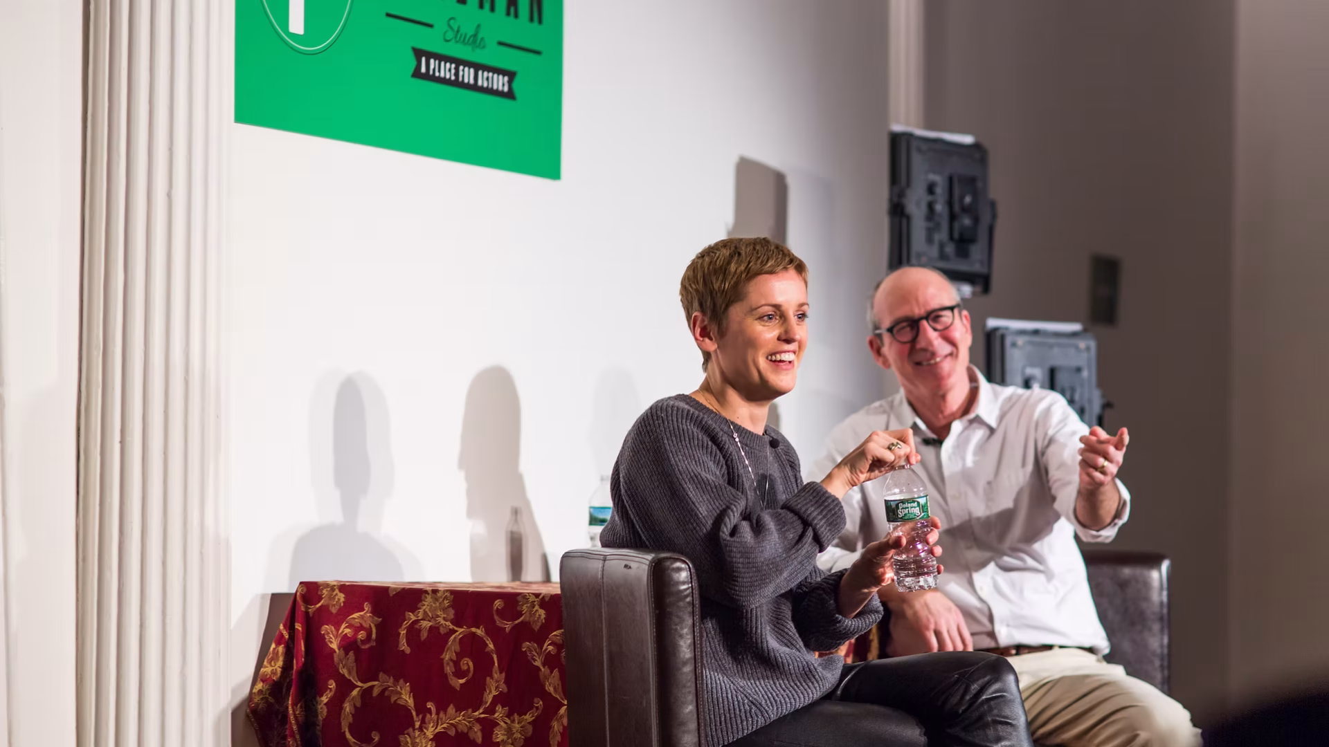 The Freeman Studio A woman and a man sit on stage in conversation at an event, with a green "The Freeman Studio" sign—known as a top New York Acting Studio—displayed on the wall behind them. New York & Toronto Acting Studio